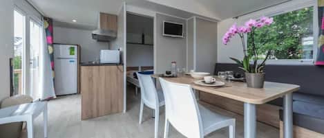A modern kitchen with a dining area, a TV mounted above the counter, and a potted orchid on the table.