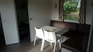 Een compacte kamer met een kitchenette, een zithoek met twee witte stoelen en een raam met gordijnen.
