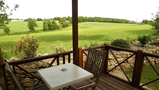 Een houten terras met een tafel en stoelen, uitkijkend op een groen veld.