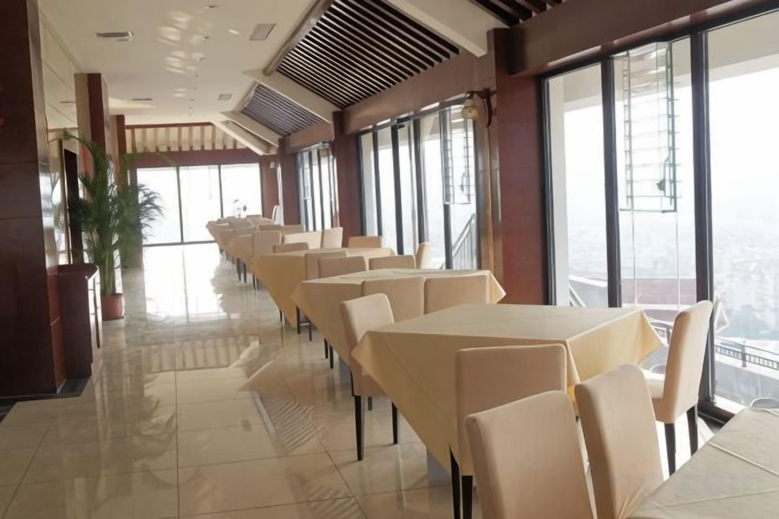 Een restaurant met lange tafels en stoelen, grote ramen en uitzicht op de stad.