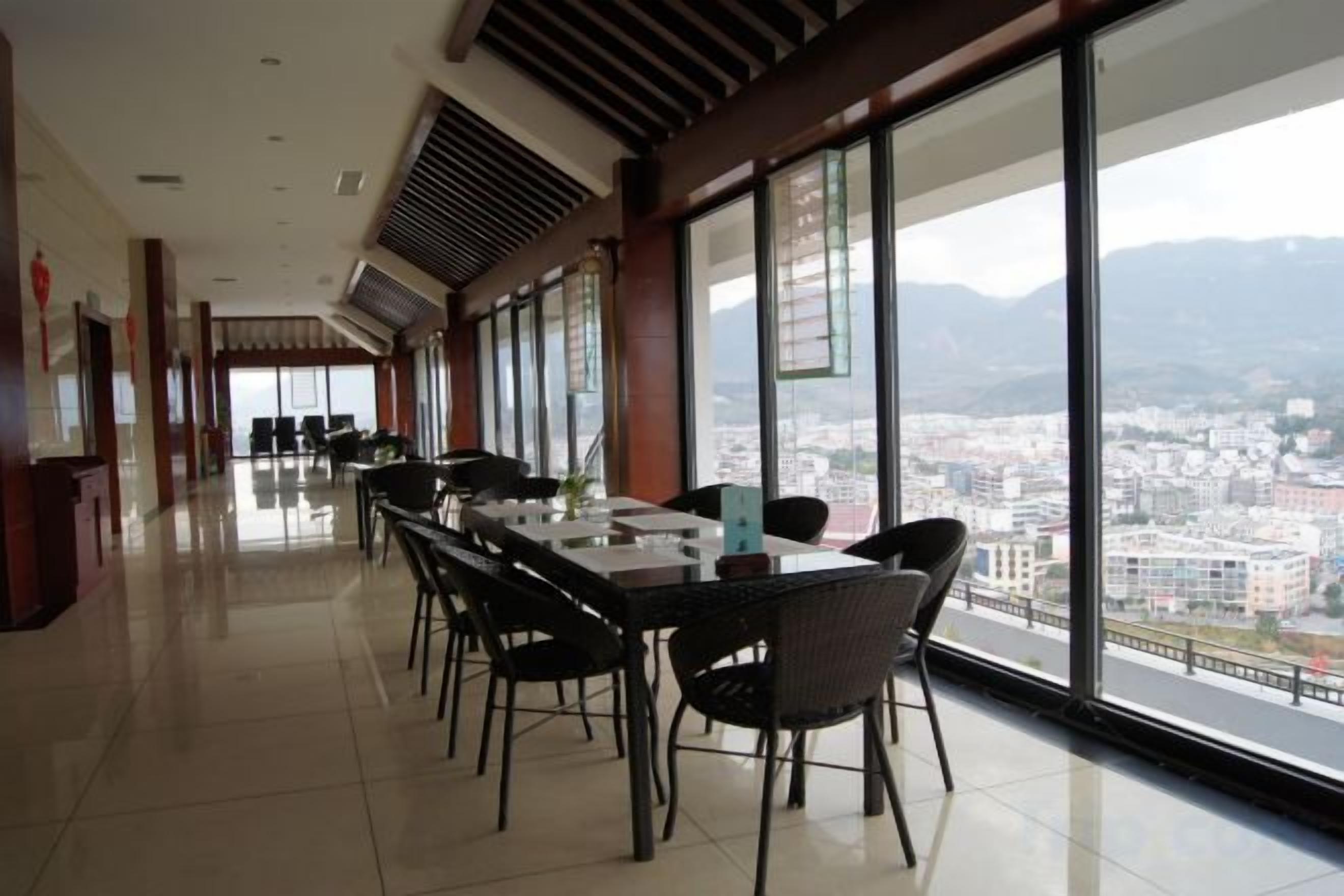 A long dining area with tables and chairs, large windows with a city view, and a high ceiling with ventilation.