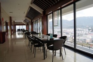Un comedor amplio con mesas y sillas, ventanas grandes con vista a la ciudad y un techo alto con ventilación.