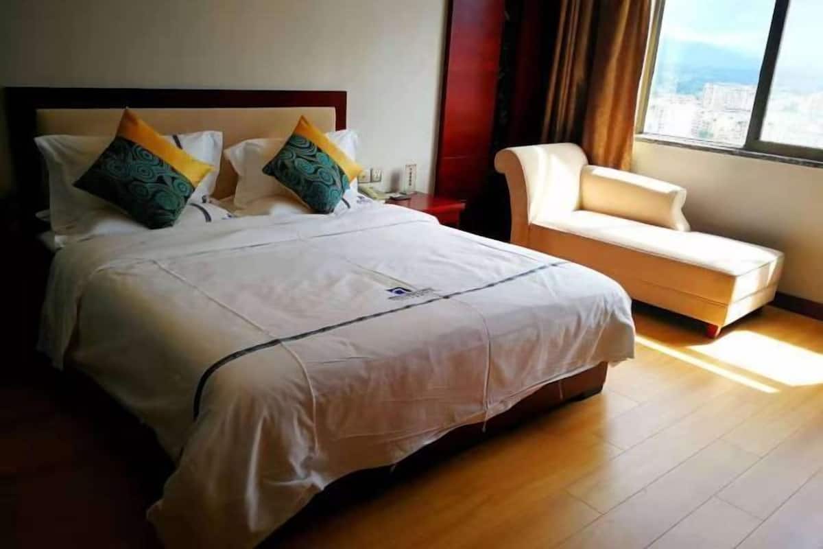 A hotel room with a bed, a sofa, a window with a city view, and a wooden floor.