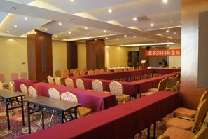 Une salle de conférence avec des rangées de tables et de chaises, un sol recouvert de moquette et une porte visible au fond.