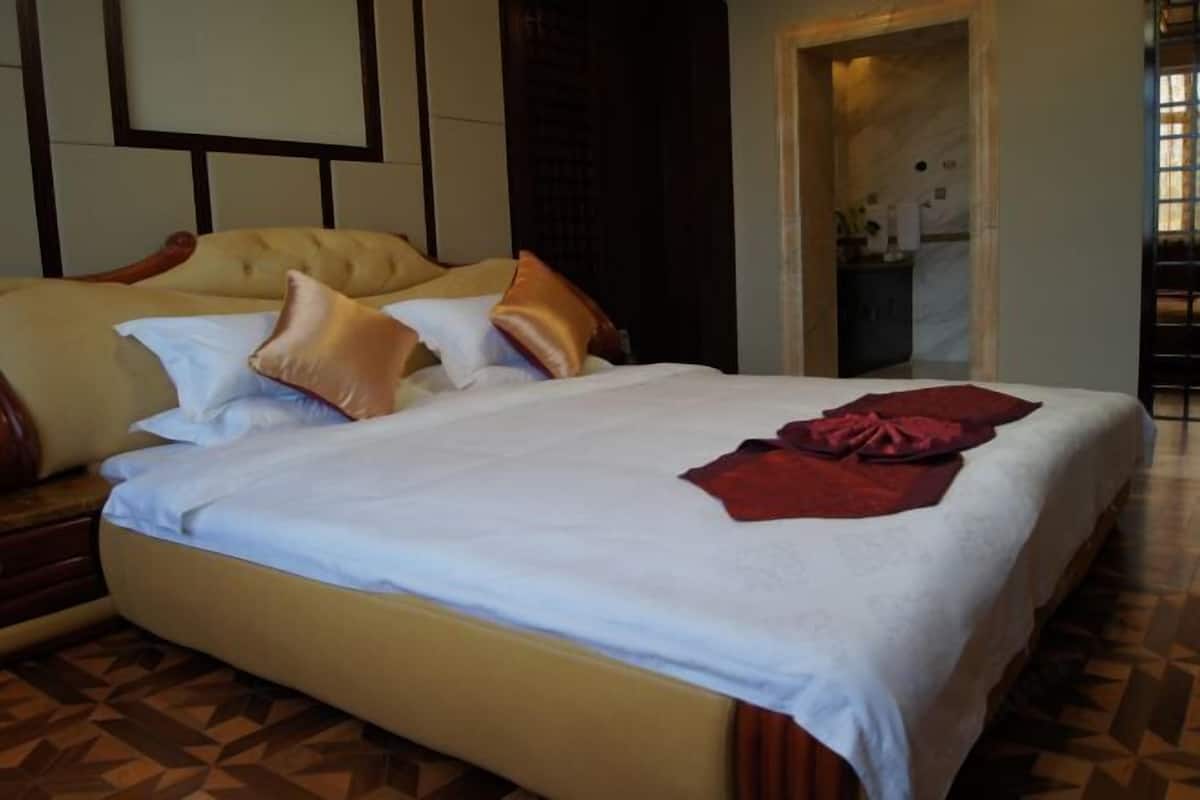 A bed with a white bedspread and multiple pillows, a wooden headboard, and a patterned floor.
