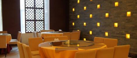 Un espace repas avec des tables et des chaises rondes, un mur décoratif agrémenté de luminaires et une grande fenêtre ornée d’un motif en treillis.