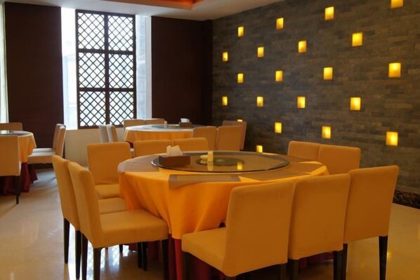 Un espace repas avec des tables et des chaises rondes, un mur décoratif agrémenté de luminaires et une grande fenêtre ornée d’un motif en treillis.