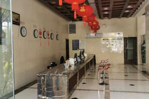 Un espace d’accueil avec un comptoir en marbre, des décorations rouges suspendues, des horloges et une affiche au mur.