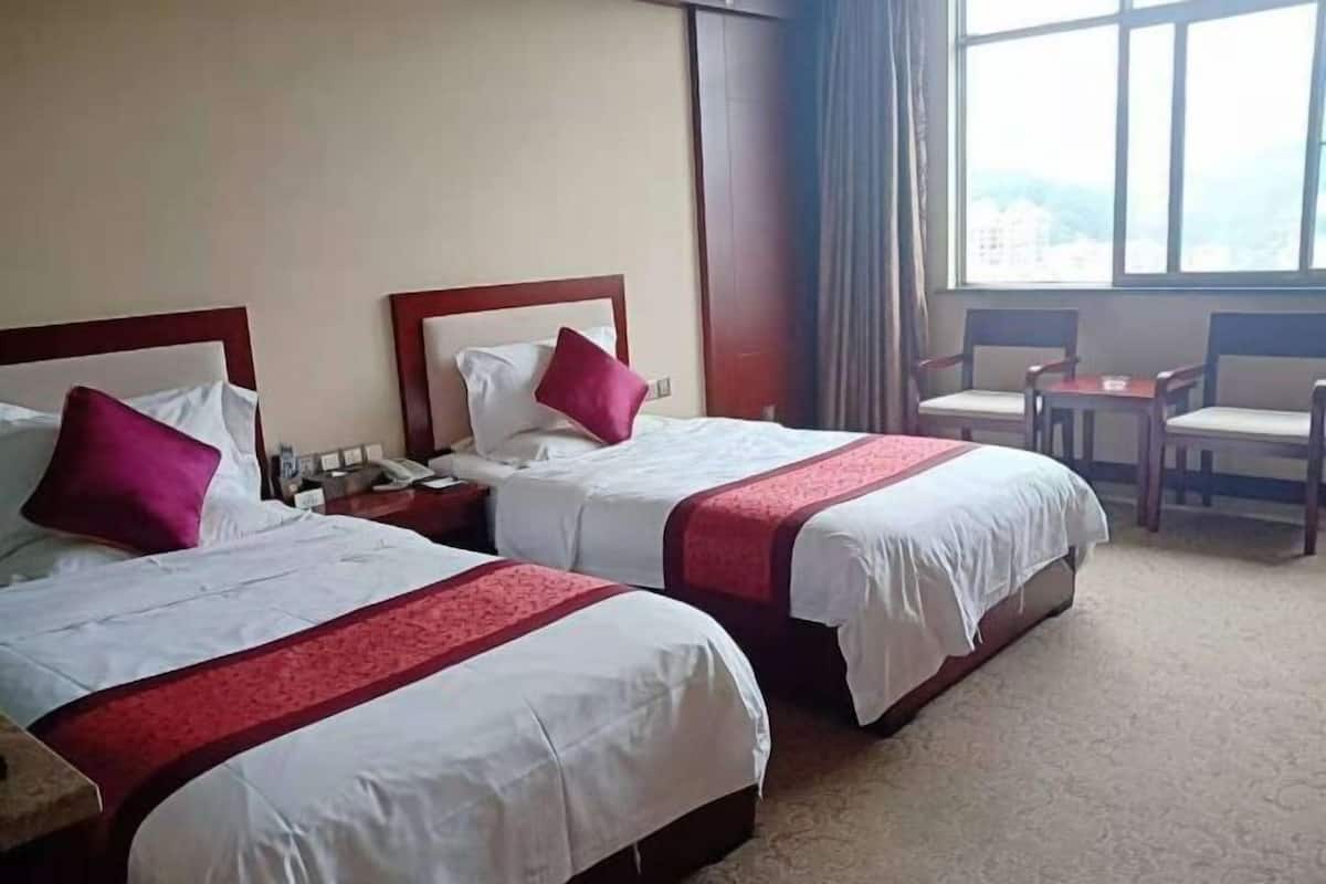 A hotel room with two beds, a small table, and a chair.