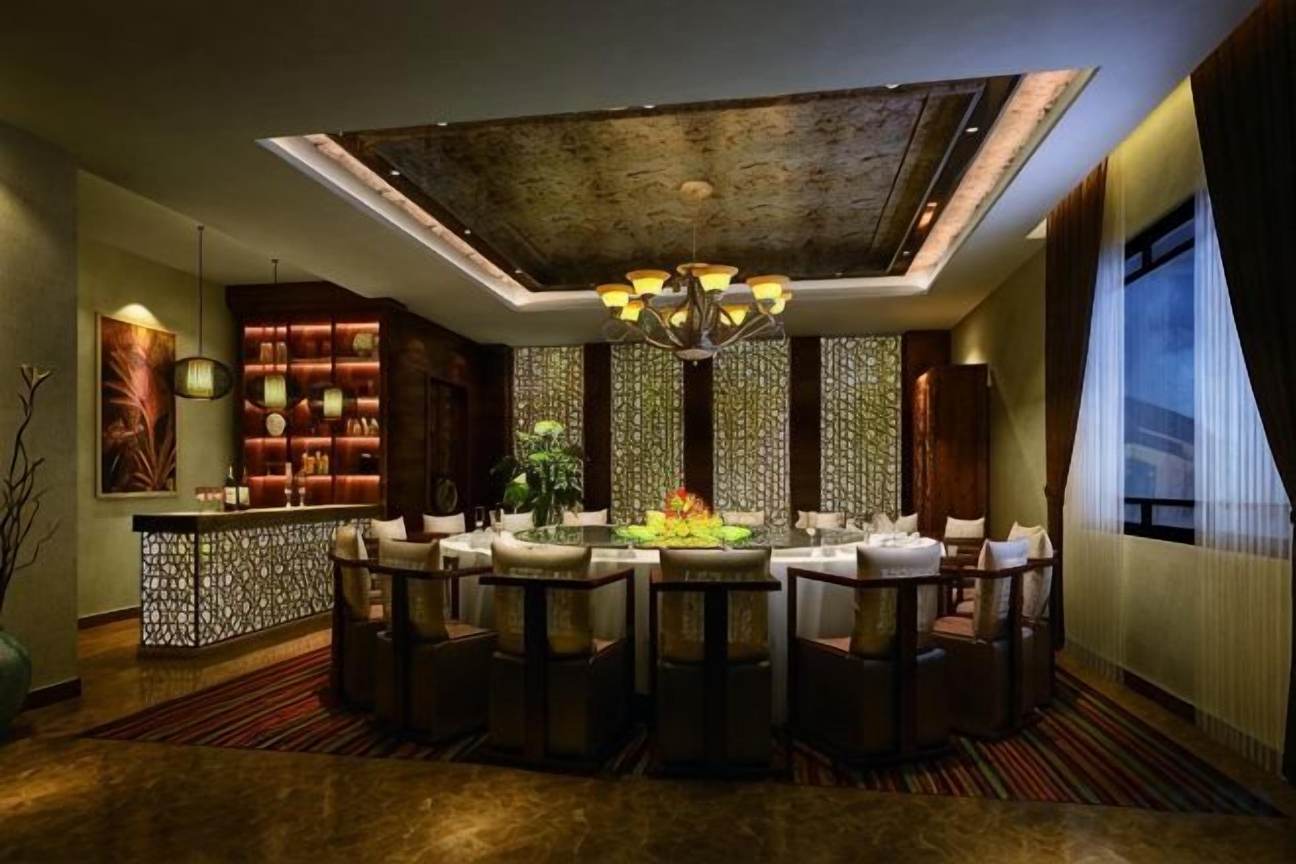Uma sala de jantar com uma mesa central, cadeiras, um candelabro e uma parede decorativa com painéis verticais.