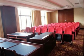 Une salle de conférence avec des rangées de chaises et de tables rouges, de grandes fenêtres avec des rideaux et un tapis à motifs.