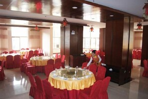 A banquet hall with round tables covered in yellow tablecloths, red chairs, and a person arranging tables.