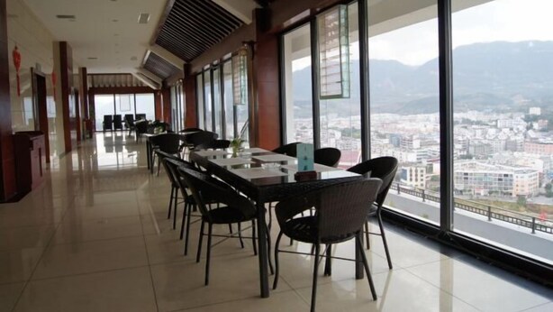 A dining area with a long table and chairs, large windows with a city view, and a modern interior design. - Weiyuan River International Hotel (Jinggu)