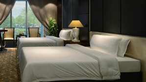 A hotel room with two beds, a desk, a chair, a lamp, and a view of the outdoors. - Weiyuan River International Hotel (Jinggu)