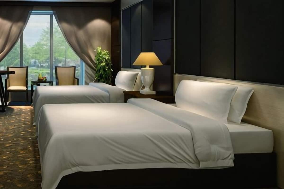 A hotel room with two beds, a desk, a chair, a lamp, and a view of the outdoors.
