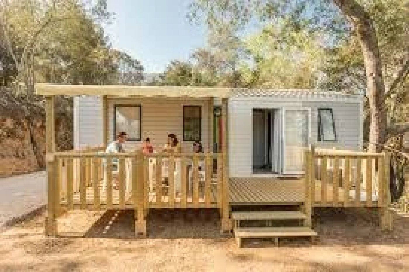 Uma cabana pequena com varanda e alpendre coberto, rodeada por árvores.