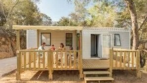 Une petite cabane dotée d’une terrasse et d’un porche abrité, entourée d’arbres.