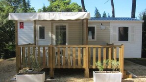 Ein kleines, eingeschossiges Mobilheim mit Holzterrasse und zwei Blumentöpfen.