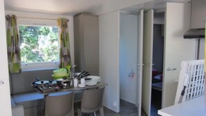 Eine kleine Küche mit Essbereich, einem Fenster mit Vorhängen und Blick auf Grünfläche.