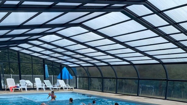 Ein Hallenbad mit klarem Wasser, umgeben von Liegestühlen und einer überdachten Dachkonstruktion.