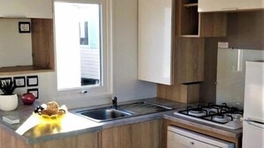 Une cuisine compacte avec des meubles en bois, un lave-vaisselle encastré, une cuisinière à gaz et une fenêtre qui laisse entrer la lumière naturelle.