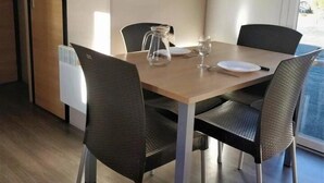 Un coin repas avec une table en bois, quatre chaises, un pichet et un extincteur fixé au mur.