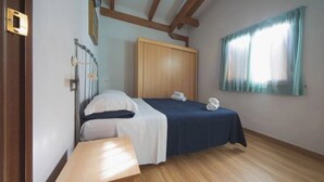 Un dormitorio con cama, mesita de noche de madera, armario y ventana con cortinas.