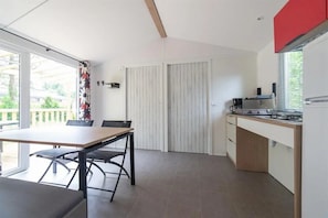 Une cuisine moderne avec un coin repas, comprenant une grande table et des chaises, une cuisinière encastrée et une fenêtre avec des stores.