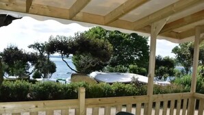 Un espacio al aire libre cubierto con una mesa y sillas, con vistas a un cuerpo de agua y vegetación.