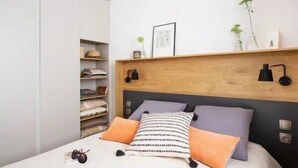 Un dormitorio moderno con una cama, almohadas, una estantería con objetos decorativos y una lámpara de pared.