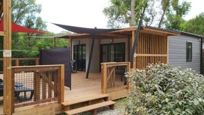 A wooden deck with a covered seating area, a fenced play area, and a small building with a gray exterior.