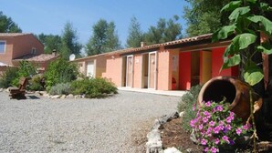 A building with a gravel driveway, a wooden bench, and a large planter with pink flowers.
