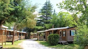 A row of wooden cabins with balconies, surrounded by trees and a gravel path.
