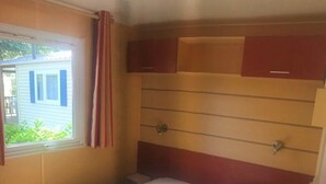 A small, single-bed room with a window, a bed with a floral bedspread, and a red headboard.