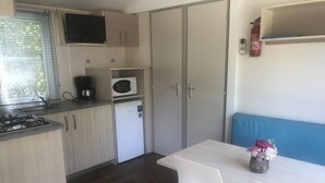 Cocina compacta con microondas, estufa y lavaplatos. Incluye un refrigerador pequeño y una zona de comedor con una mesa y una silla.
