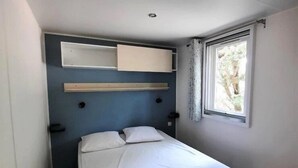 Un dormitorio pequeño y moderno con una cama individual, cabecera integrada, ventana con cortinas e iluminación en el techo.