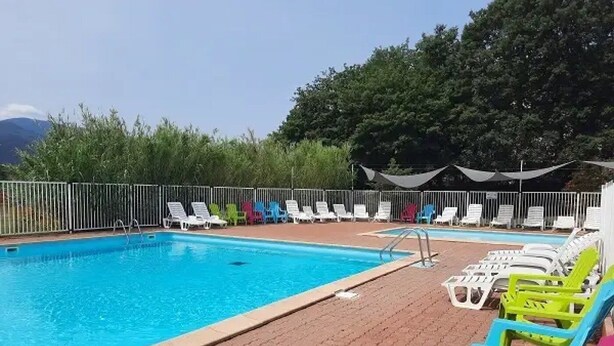 Una piscina con sillones blancos y coloridos, rodeada por una valla y árboles.
