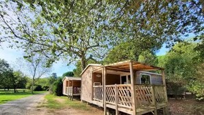 Alojamiento de estilo rústico tipo cabaña, con terraza de madera y porche cubierto, rodeado de exuberante vegetación.