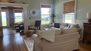 Un salón amplio con un sofá beige grande, una mesa de centro de madera y vista al océano a través de amplias ventanas.