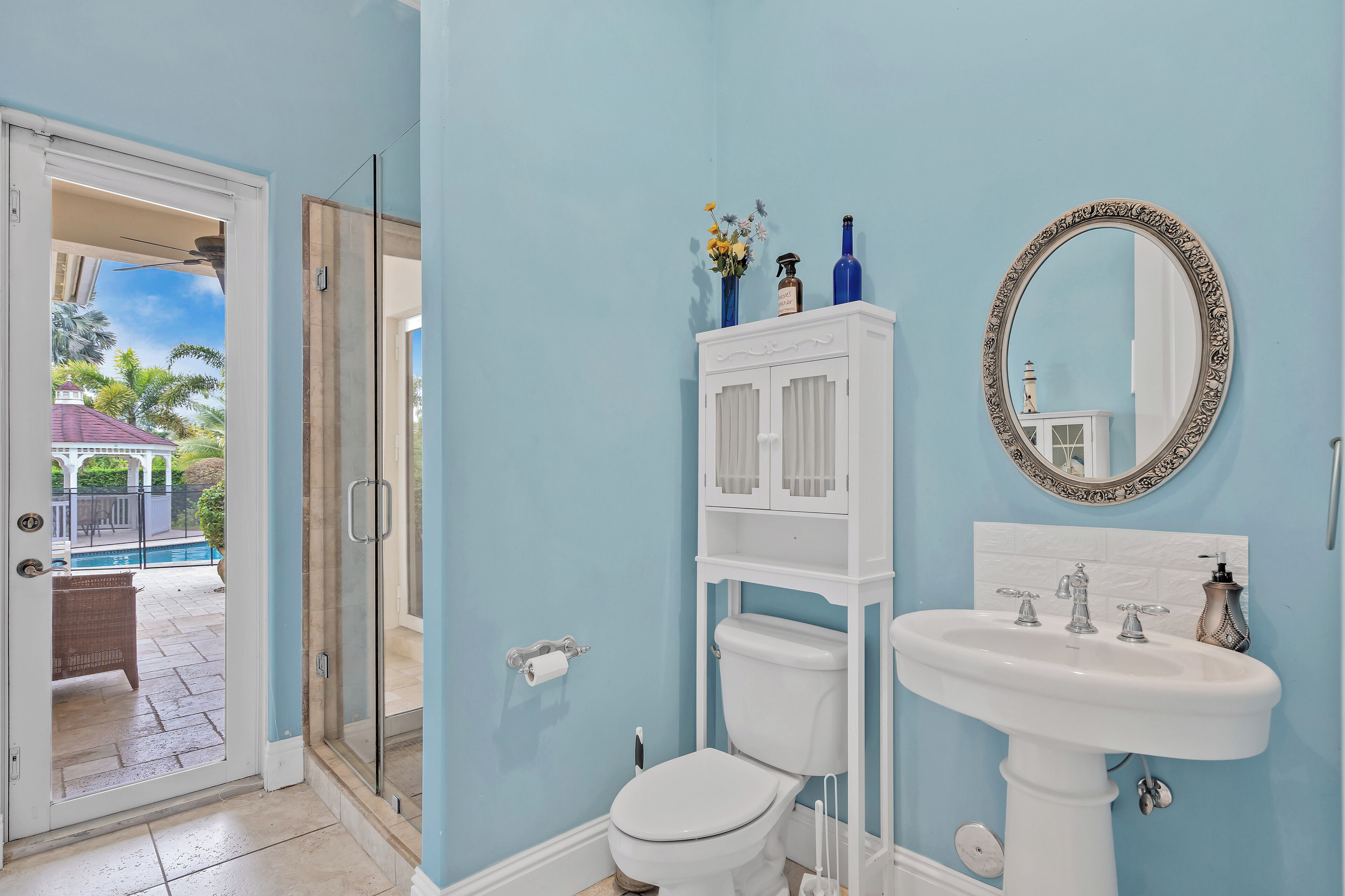 Un baño con lavamanos, inodoro y ducha blancos. Se observa un espejo con un marco ornamentado y un mueble con objetos decorativos.