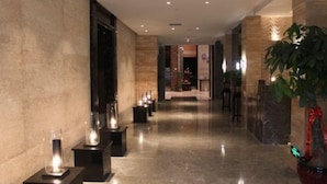 A corridor with a polished marble floor, walls with a textured pattern, and a potted plant on the right. - Gurun Eco Hotel (Luoyuan)