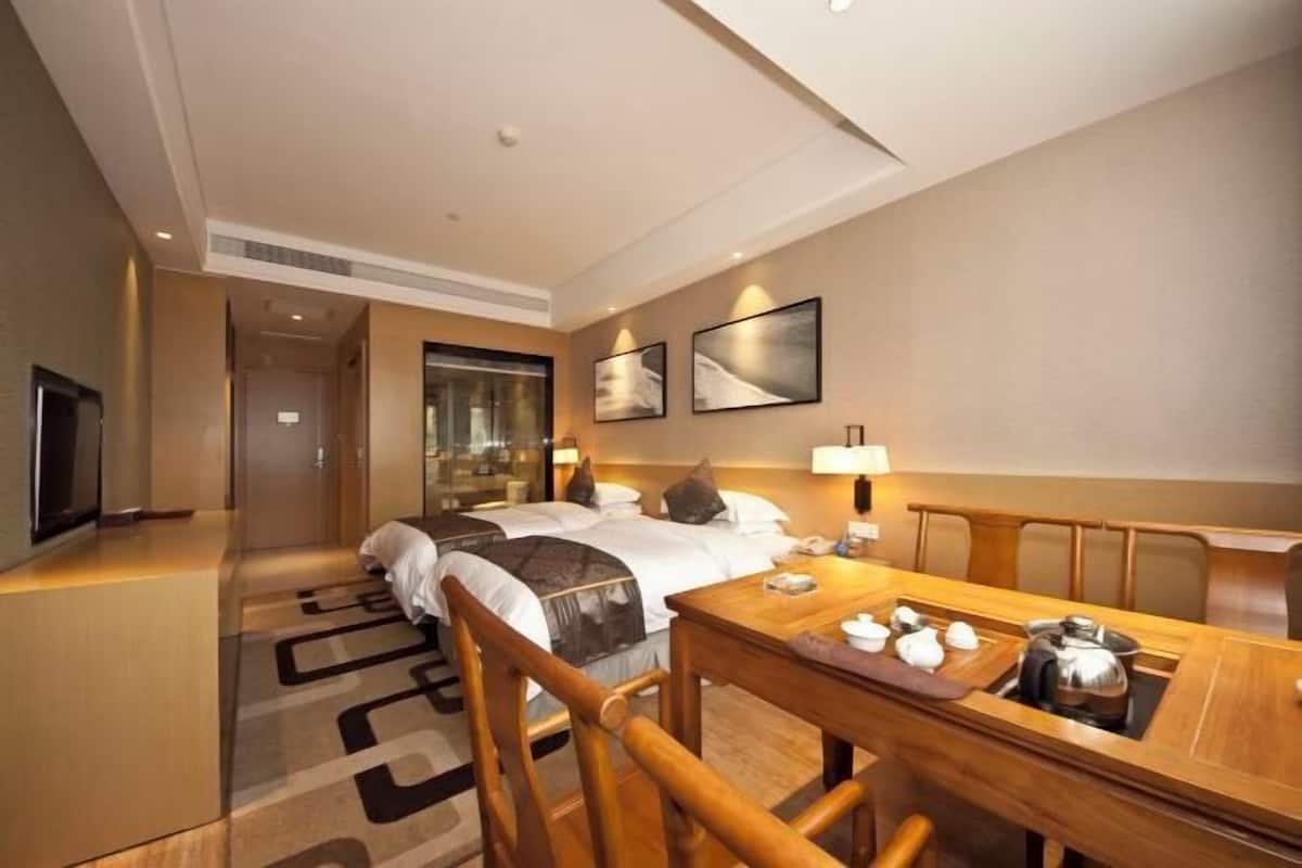 Una habitación de hotel con una cama, un escritorio con tetera, una televisión y obras de arte enmarcadas en la pared.