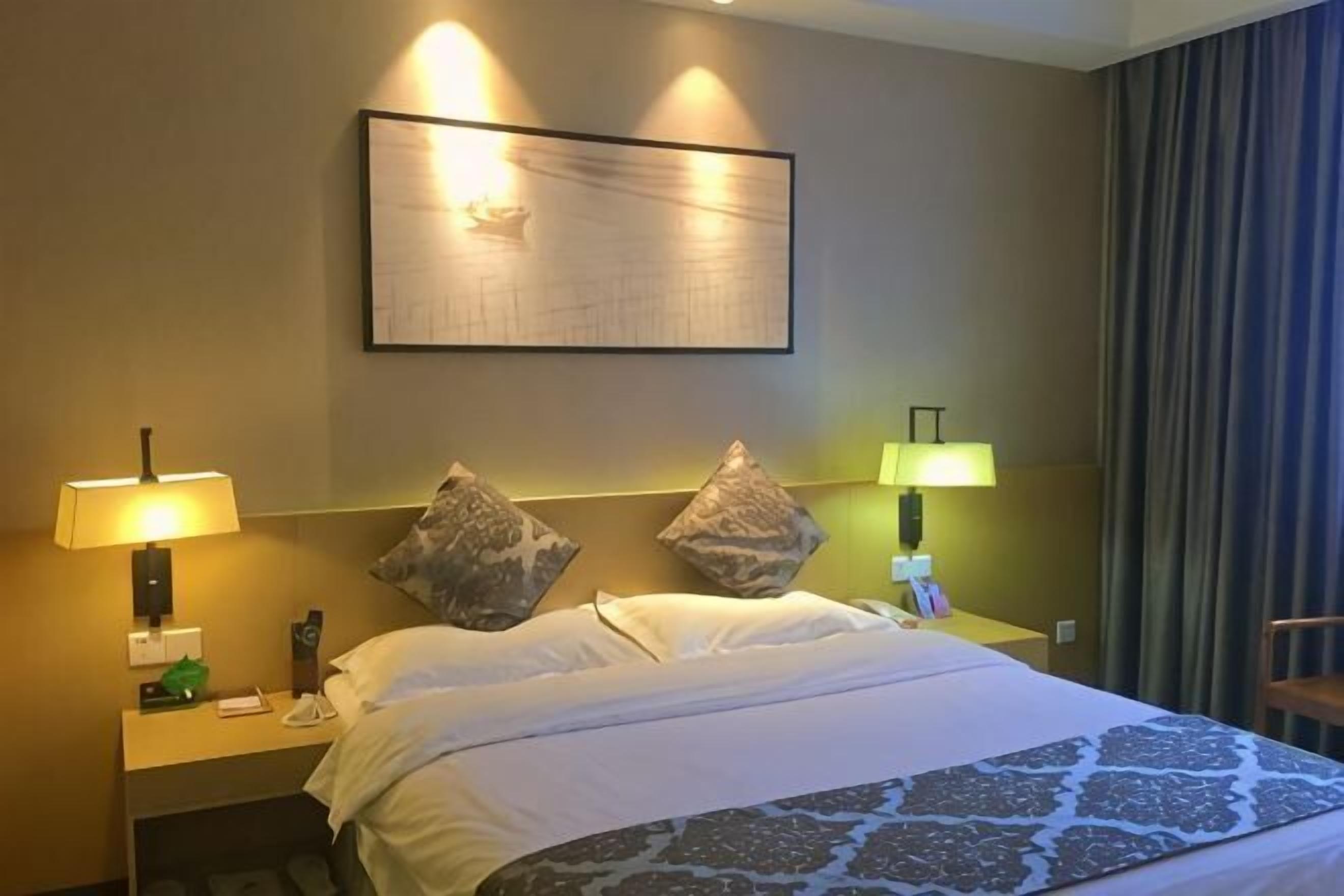 Une chambre d’hôtel avec un grand lit, deux lampes de chevet, une œuvre d’art encadrée au-dessus du lit et une chaise près de la fenêtre.