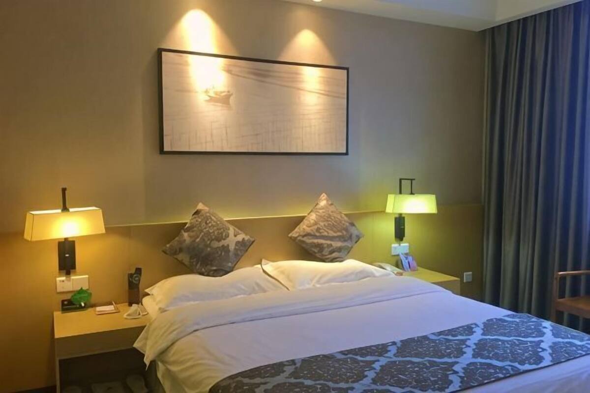 Habitación de hotel con una cama grande, dos lámparas de noche, un cuadro enmarcado sobre la cama y una silla junto a la ventana.