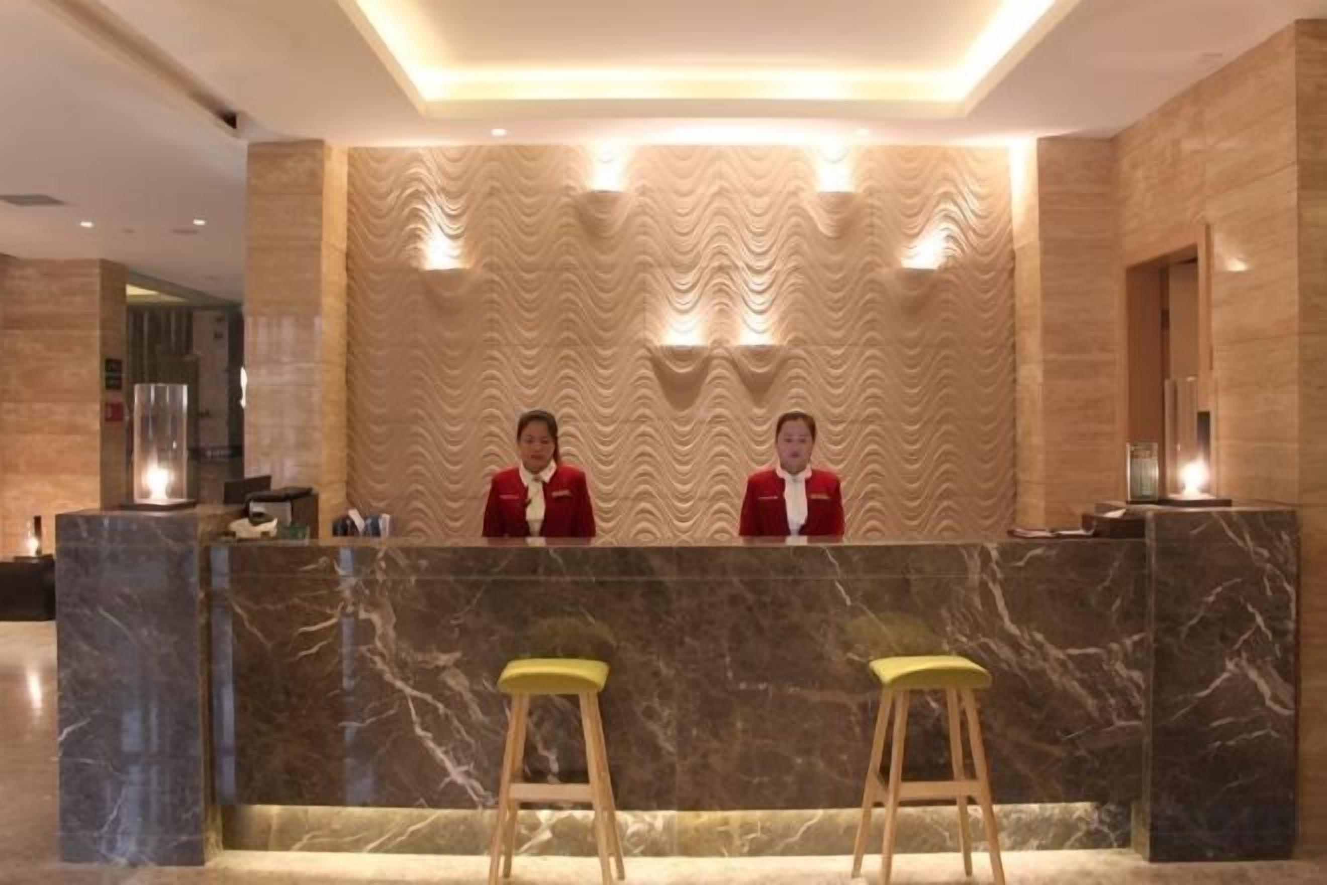 A reception desk with two staff members, a marble counter, and two stools.
