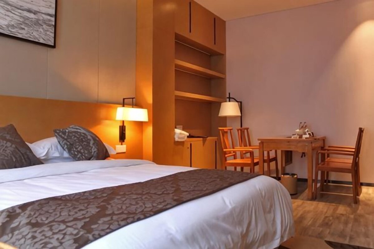 A hotel room with a bed, bedside lamps, a desk with chairs, and a small table.