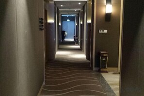 Un pasillo de hotel con piso alfombrado, luces en la pared y una puerta al final.