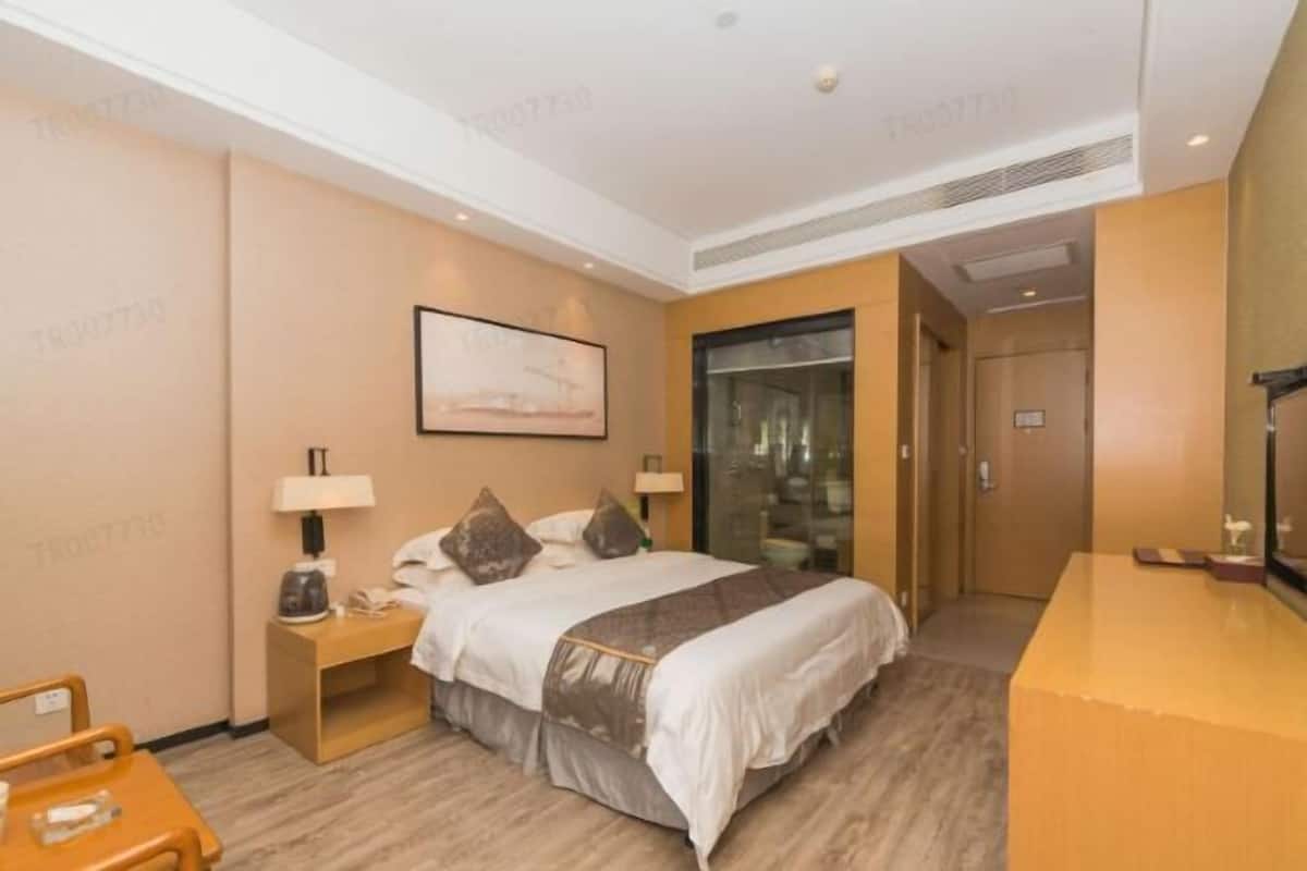 Una habitación de hotel con cama, mesitas de noche, un escritorio, una silla, un espejo grande y una puerta que da al baño.