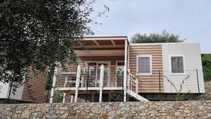 Une maison moderne à deux étages, avec des fondations en pierre, un balcon doté d’une rambarde en métal et une terrasse en bois.