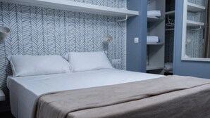 Ein ordentlich bezogenes Bett mit grauer Decke, einem weißen Kopfkissen und einer weißen Daunendecke in einem Zimmer mit Zickzack-Papier und einem Einbauschrank mit Kleiderstange.